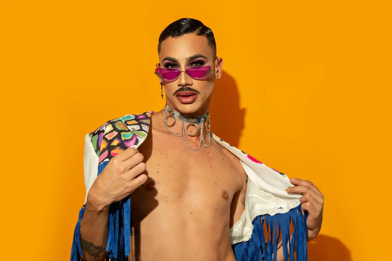 A performer in a sequinned outfit and pink sunglasses against an orange backdrop