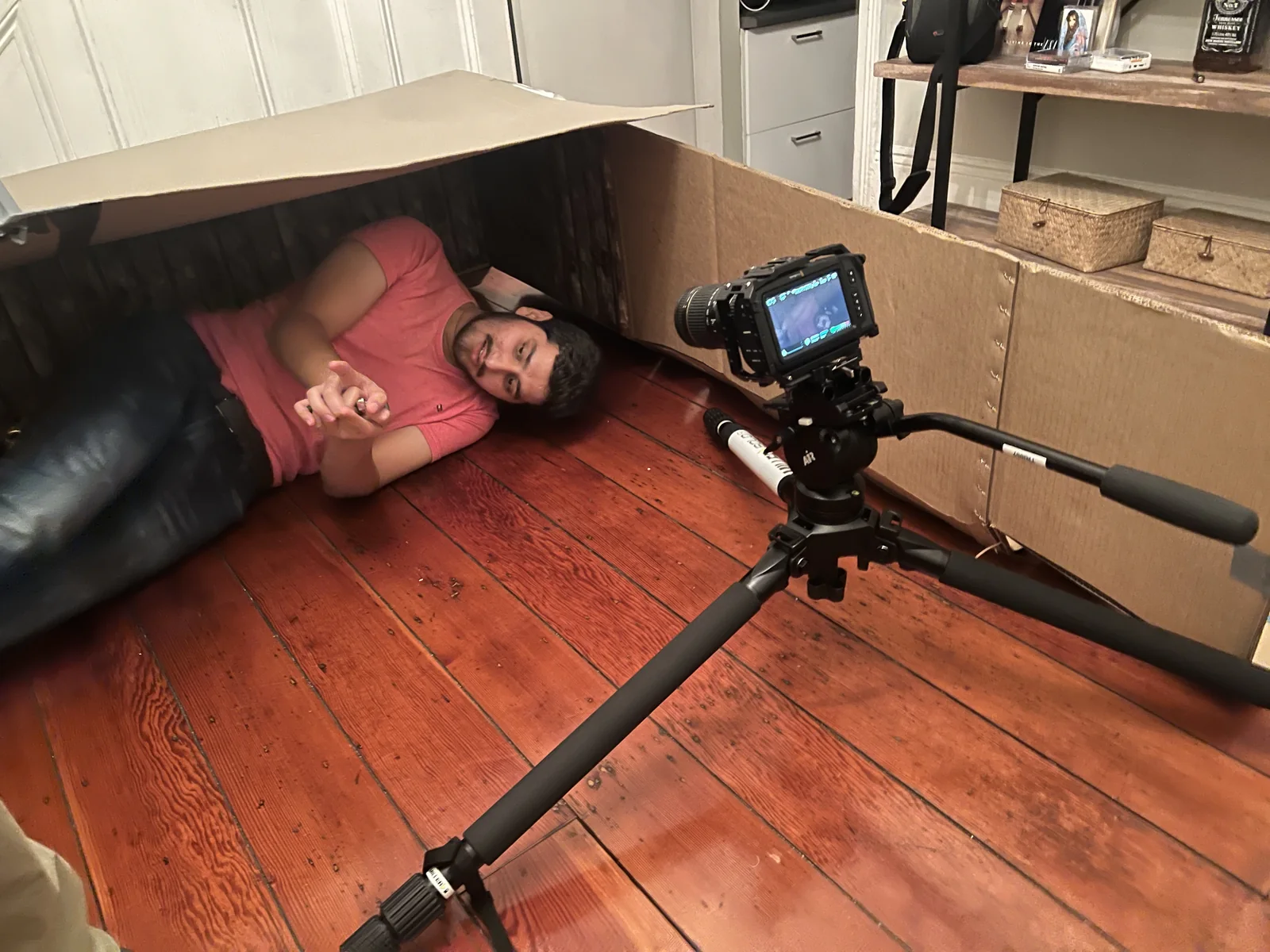 Bastidores: o ator deitado no caixão de papelão, com uma câmera de cinema num tripé lá dentro