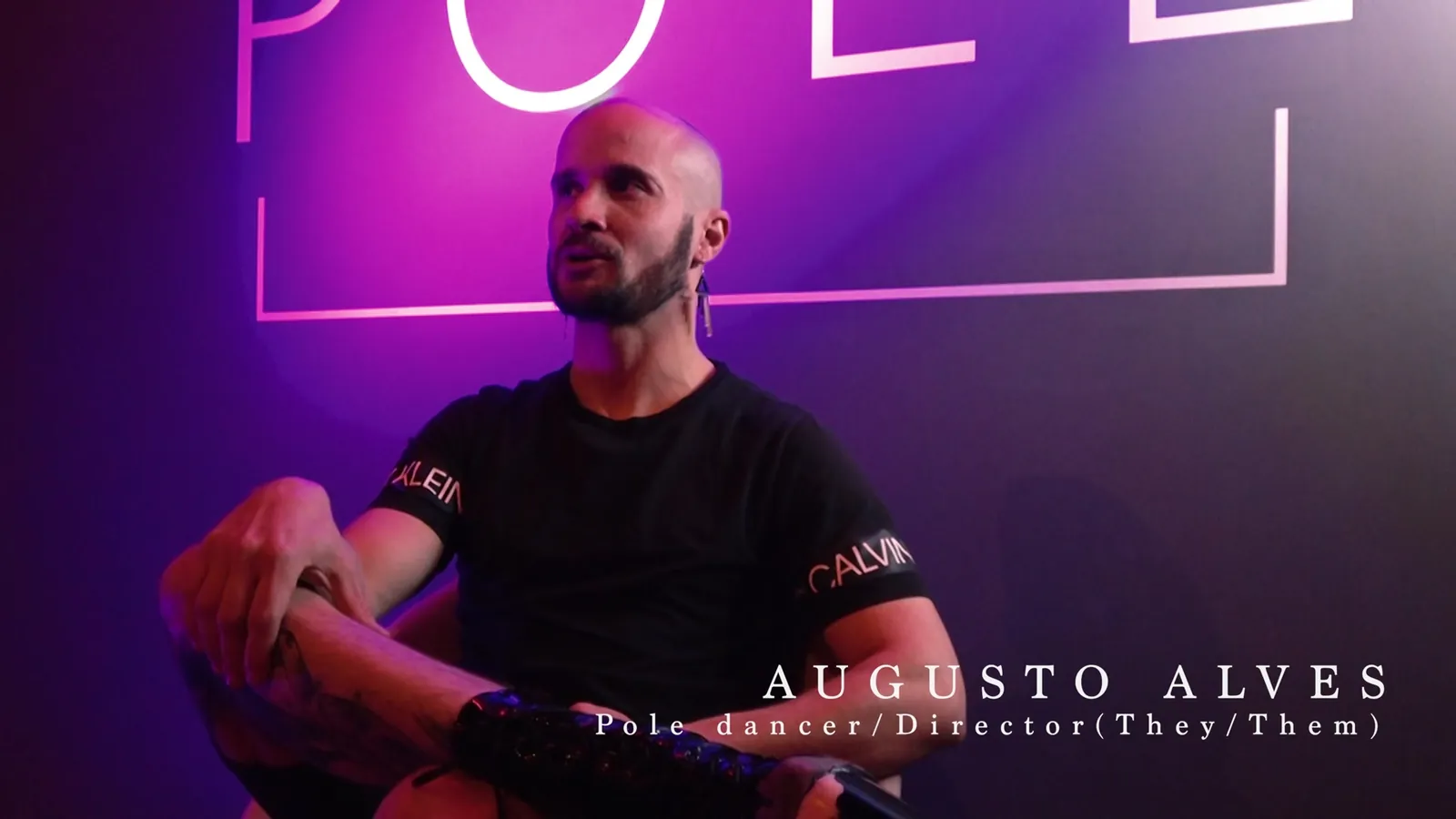 Augusto Alves in interview under a pink neon sign, captioned pole dancer and director