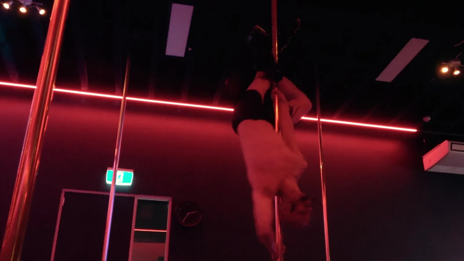 A dancer hangs upside down from the pole in a red-lit studio