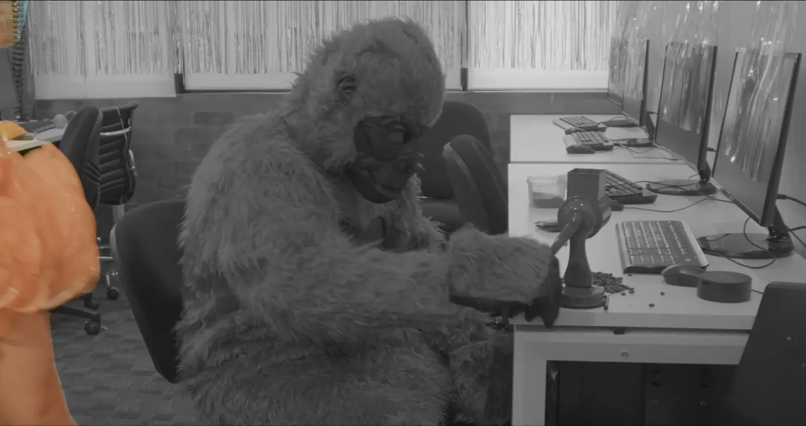 A person in a gorilla costume sits at an office desk