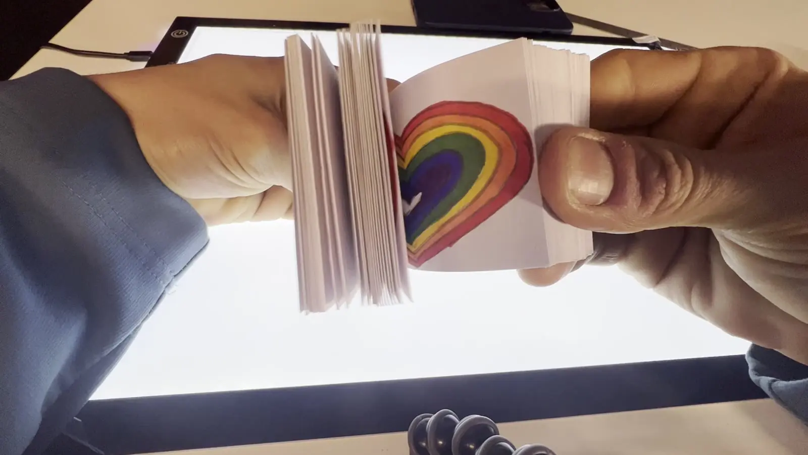 Mãos folheando um pequeno flipbook com um arco-íris desenhado