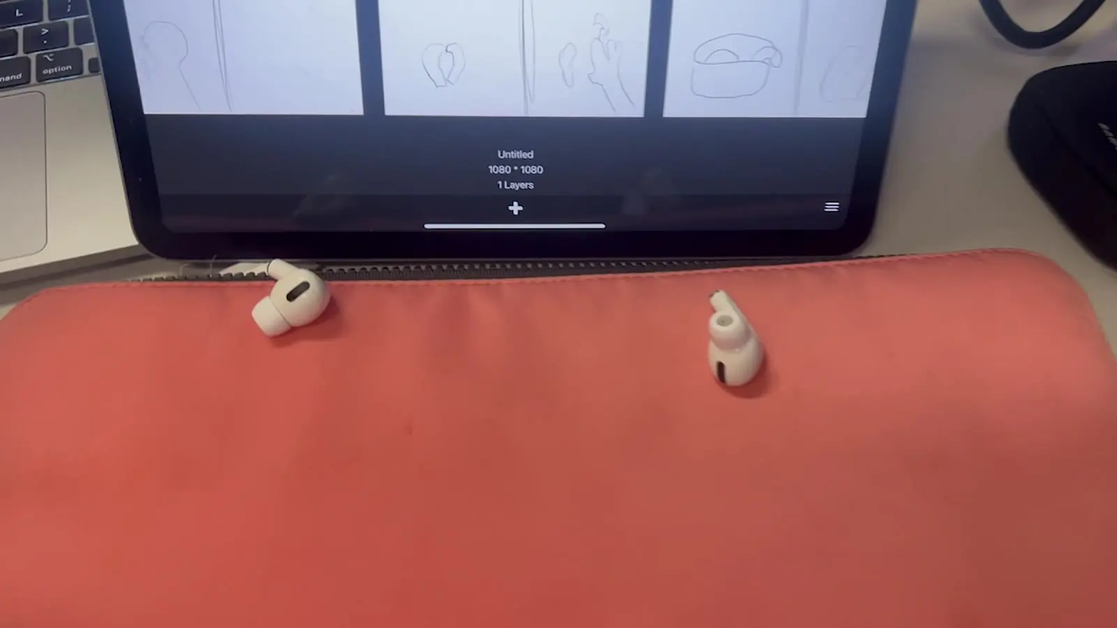Fones de ouvido sem fio brancos sobre um mousepad coral, na frente de um tablet